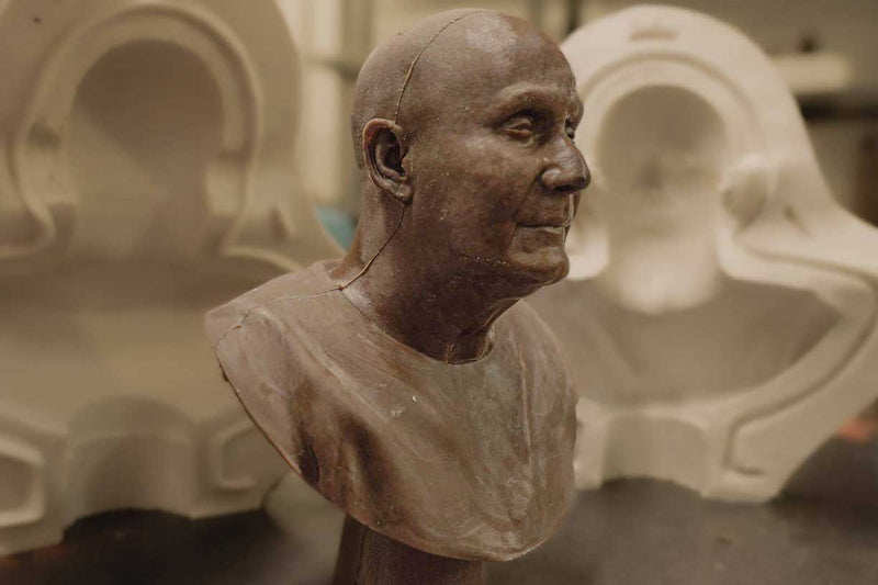 The picture shows a wax copy of a rare bronze sculpture called Compassion, depicting Sri Chinmoy. The wax sculpture is on a table with the mould of the wax sculpture in the background. 