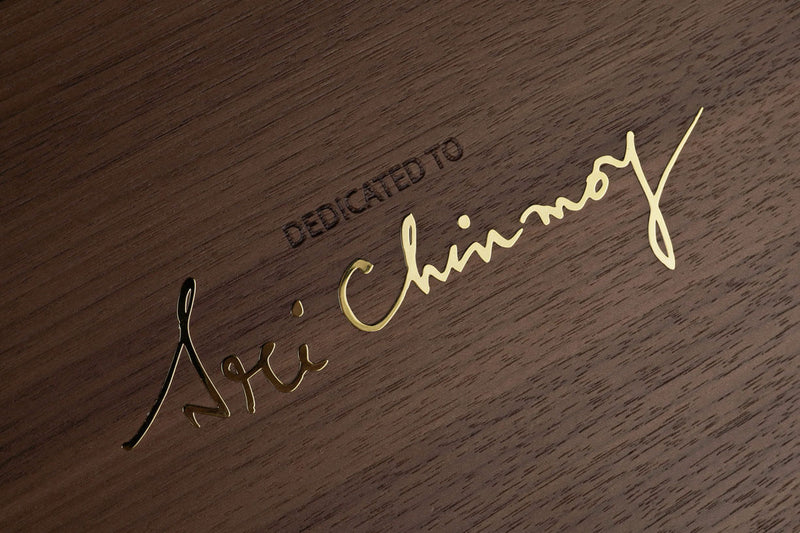 Pictured is a detail of the handcrafted walnut box for the Chinmoy Collection of luxury limited edition sculptures. The box is jeweled with gold plate inscribed with Sri Chinmoy's name in his real handwriting. Above the gold inscription, the walnut box is engraved with the inscription desicated, indicating that the product was made in his honor. The picture shows an extremely high quality luxury product.