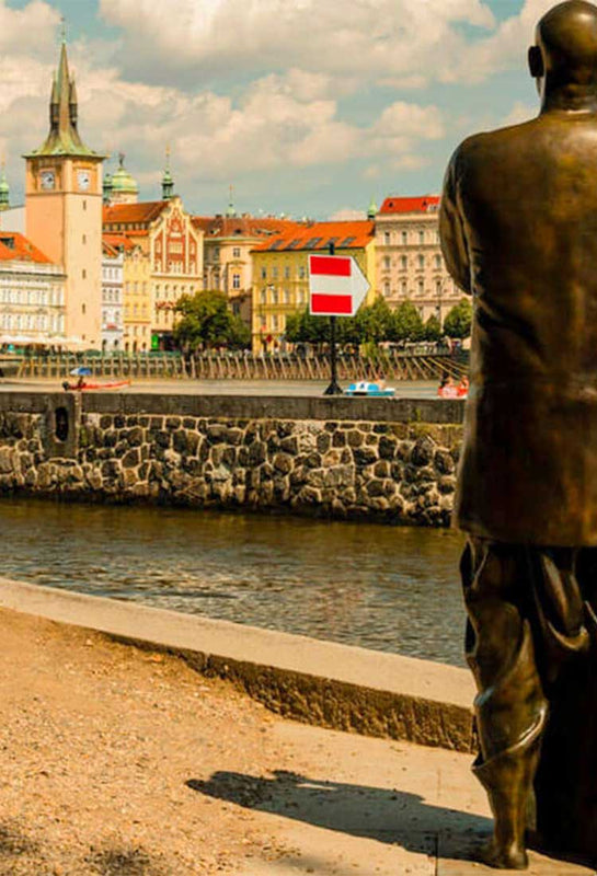Life-size statue of Sri Chinmoy on the riverbank in Prague. Prague city centre in the background