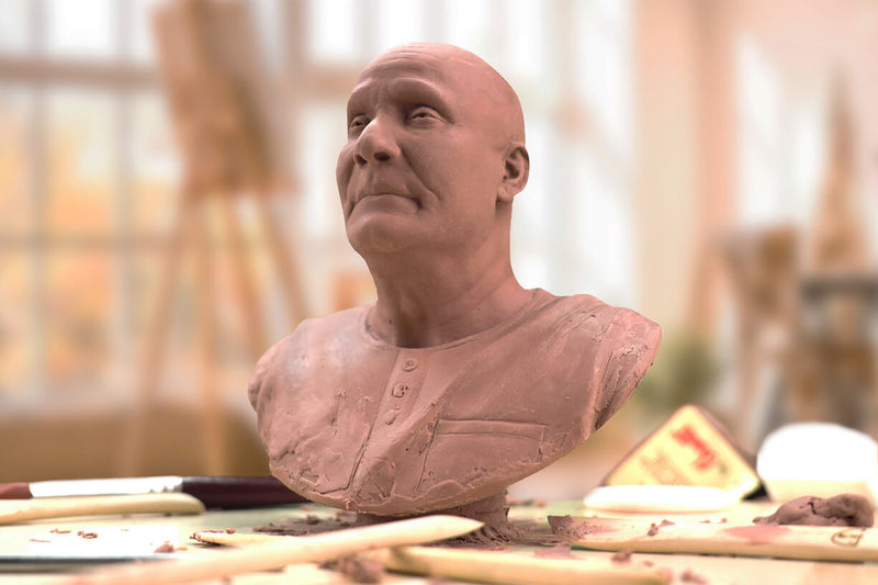 A clay replica of a rare bronze statue called Compassion, depicting Sri Chinmoy, is shown. The sculpture is on a studio table with pieces of material and sculpting props around it. In the background, the windows of the sculptor's studio are slightly blurred. The picture gives a very strong artistic impression.