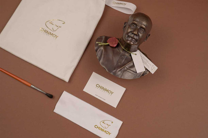 The picture shows a work of art called Compassion depicting Sri Chinmoy. Next to the statue is a care card with care instructions and a cleaning cloth. Next to it is a vegan suede dust bag from Luxury Sculptures and a dust bag.