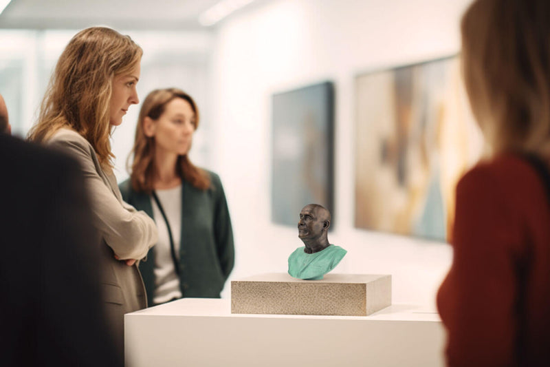 A rare art exhibition shows Compassion - a rare small bronze bust of Sri Chinmoy on a large marble plinth placed on a large white column. A group of art connoisseurs also stand around the statue and watch with great interest, starting some internal process in them. In the background, valuable paintings are displayed, which are slightly dimly visible hanging on the wall.