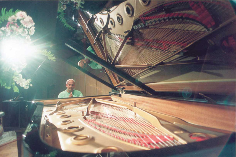 World-renowned peace ambassador and peace philosopher Sri Chinmoy sits at a large open-top piano and prays during a peace concert.