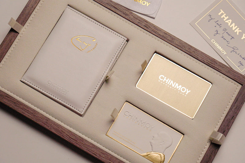 Part of the luxury packaging of the rare one-off Compassion bronze statue. An extremely elaborate wooden box insert tray with a hand-stitched vegan suede leather blade is shown, which contains a white hand-stitched faux leather ID holder, a metallic gold warranty card and a business card with recessed spaces for them.